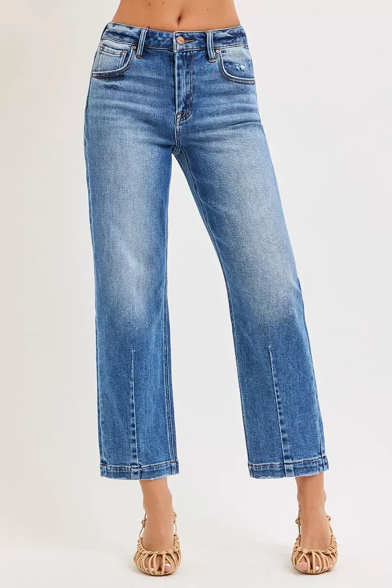 Woman wearing high-waisted straight-leg blue jeans, cropped length, neutral background
