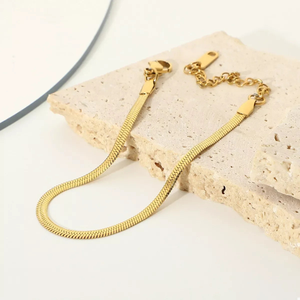 Gold herringbone chain bracelet with adjustable clasp on textured stone background