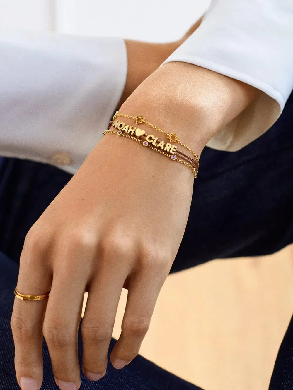 Gold personalized name bracelets with star and heart charms on woman's wrist, minimal style