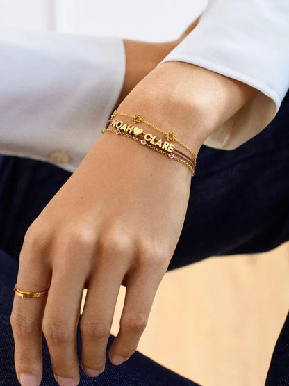 Gold personalized name bracelets with star and heart charms on woman's wrist, minimal style
