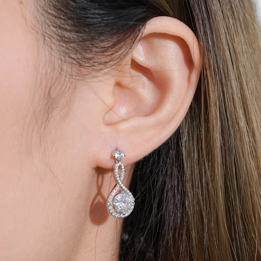 Close-up of a woman's ear wearing a silver drop earring with clear crystals.