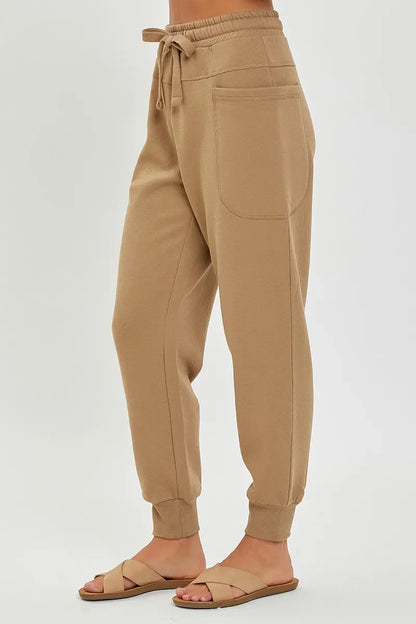 Woman wearing beige jogger pants with drawstring waist and large patch pocket, styled with sandals.