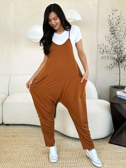 Woman wearing relaxed brown jumpsuit over white t-shirt, standing in modern living room