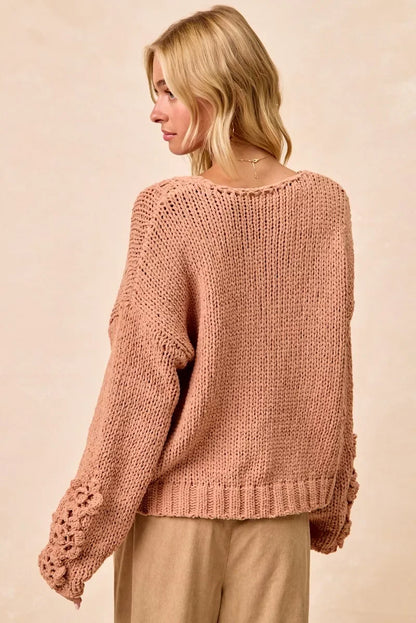 Woman wearing a loose knit blush sweater with floral sleeve details and beige trousers