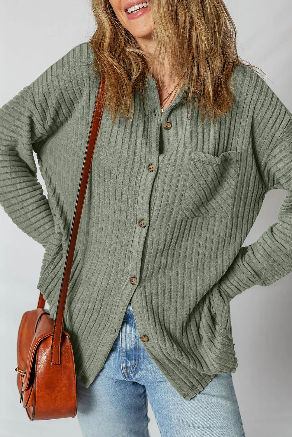 Woman wearing a ribbed sage green button-up shirt with jeans and a brown leather bag