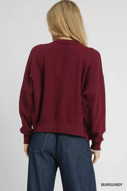 Woman wearing relaxed burgundy knit sweater with long sleeves and blue jeans, back view