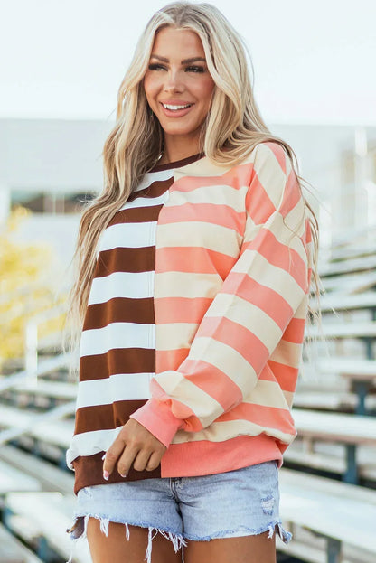 Woman wearing a colorblock striped sweatshirt with pink, cream, and brown, paired with denim shorts.