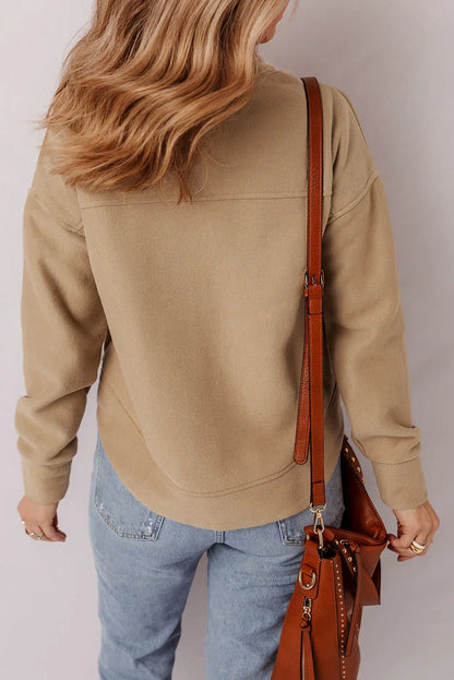 Woman in a beige pullover sweater, light wash jeans, and brown leather crossbody bag