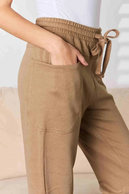 Tan drawstring jogger pants with large front pockets and relaxed fit, worn with white top
