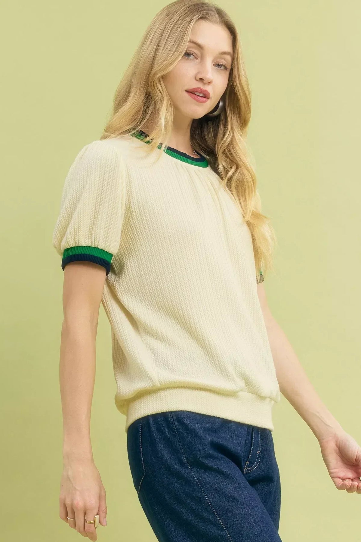 Woman wearing an ecru short sleeve knit sweater with green trim and blue jeans