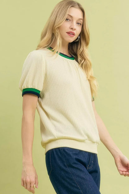 Woman wearing an ecru short sleeve knit sweater with green trim and blue jeans