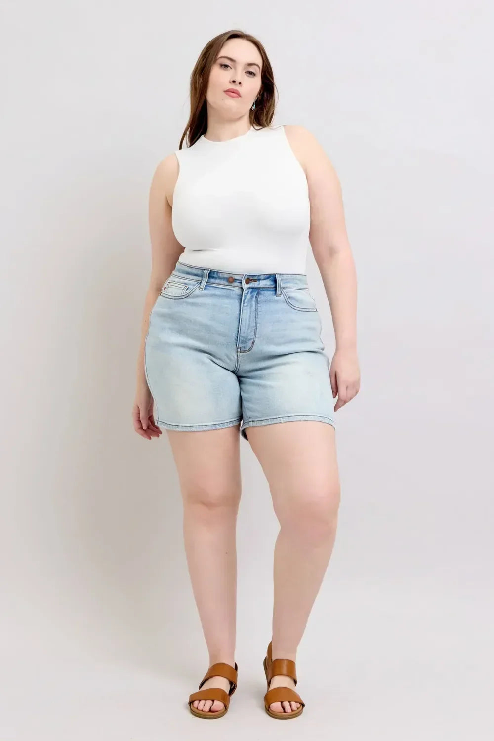 Woman in sleeveless white top and high-waisted light wash denim shorts, standing indoors