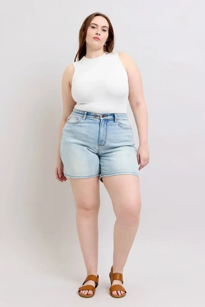 Woman in sleeveless white top and high-waisted light wash denim shorts, standing indoors