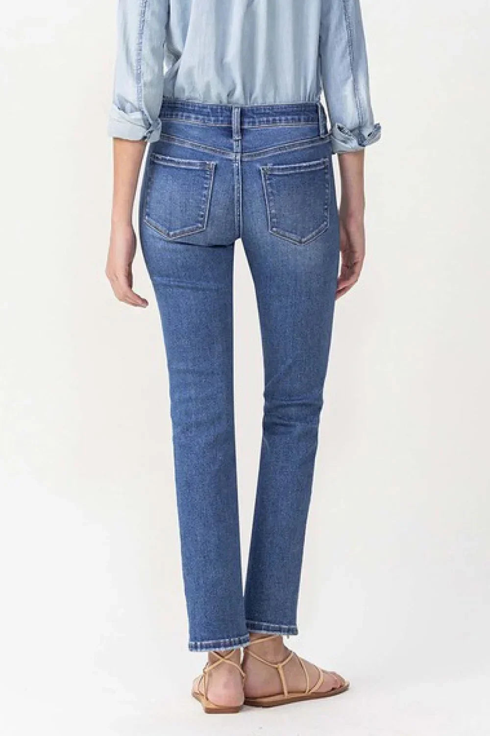Back view of woman in straight leg blue jeans, chambray shirt, and flat sandals