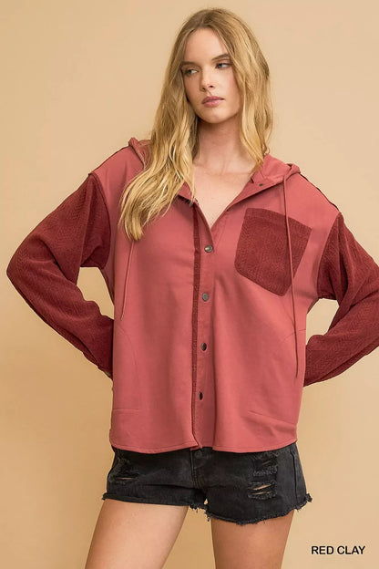 Woman wearing a red clay button-up hooded jacket with textured sleeves and black denim shorts.