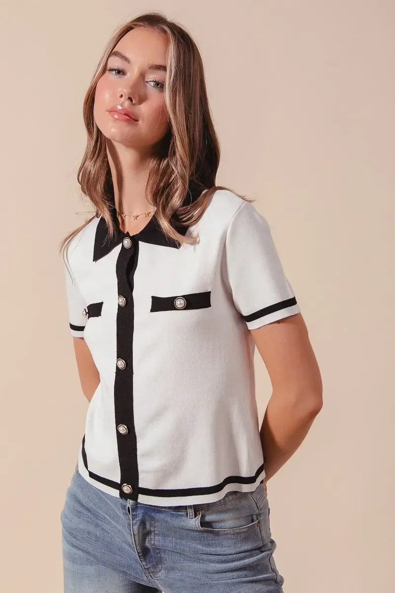 Woman wearing a short-sleeve white knit cardigan with black trim and pearl buttons