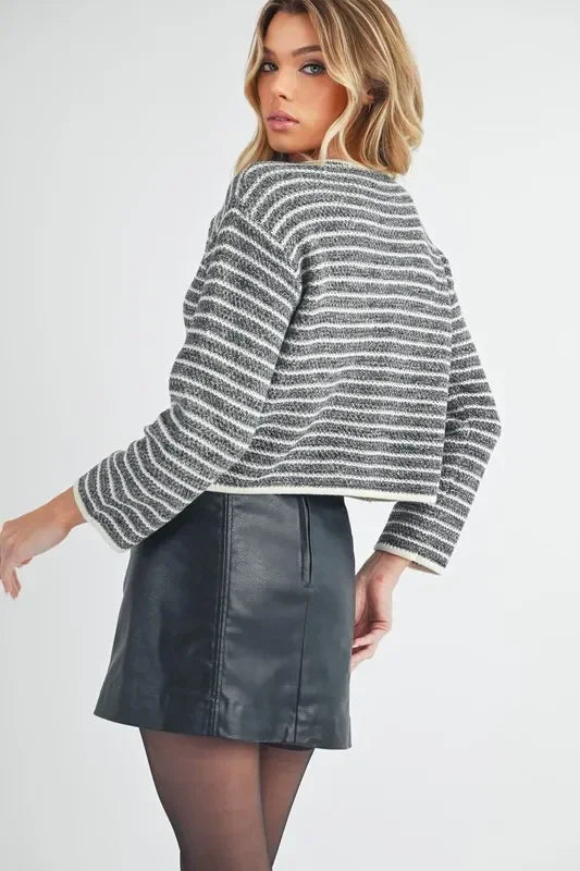 Woman wearing a black faux leather mini skirt, striped knit sweater, and sheer tights