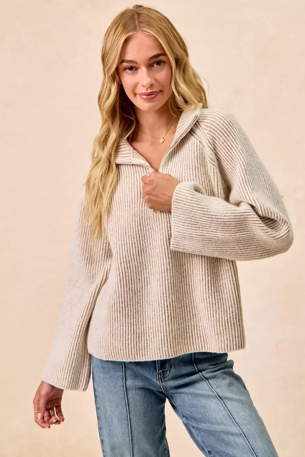 Woman wearing a ribbed beige knit pullover sweater with zipper collar and blue jeans