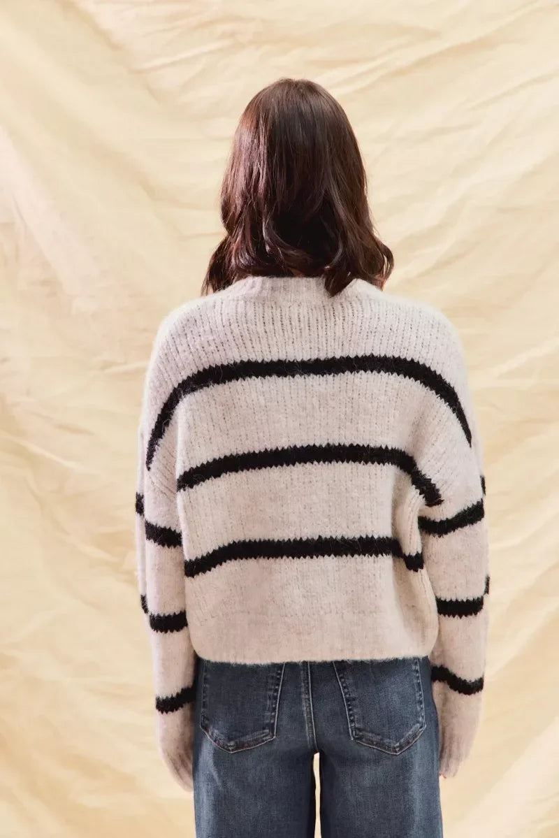 Woman wearing a cozy cream sweater with black stripes and blue high-waisted jeans, back view