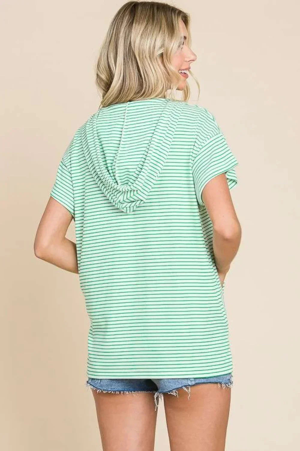 Woman wearing mint green striped short sleeve hooded top with denim shorts, back view