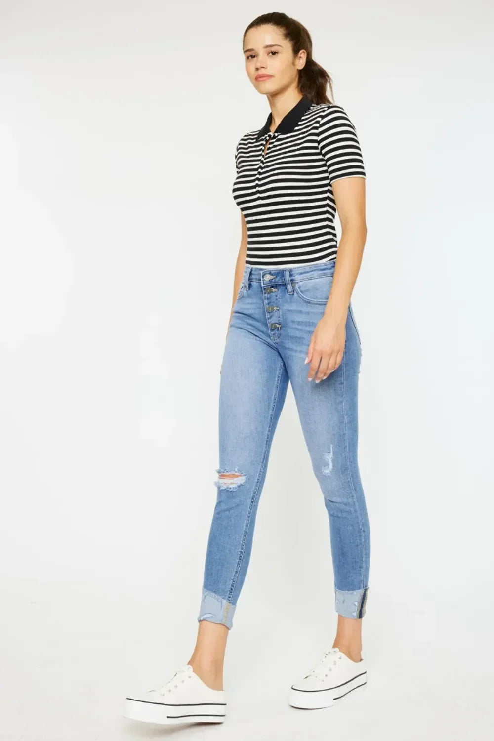 Woman wearing a black and white striped polo shirt with high-waisted distressed skinny jeans and white sneakers
