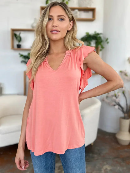 Woman wearing a coral flutter sleeve blouse and blue jeans in a modern indoor setting