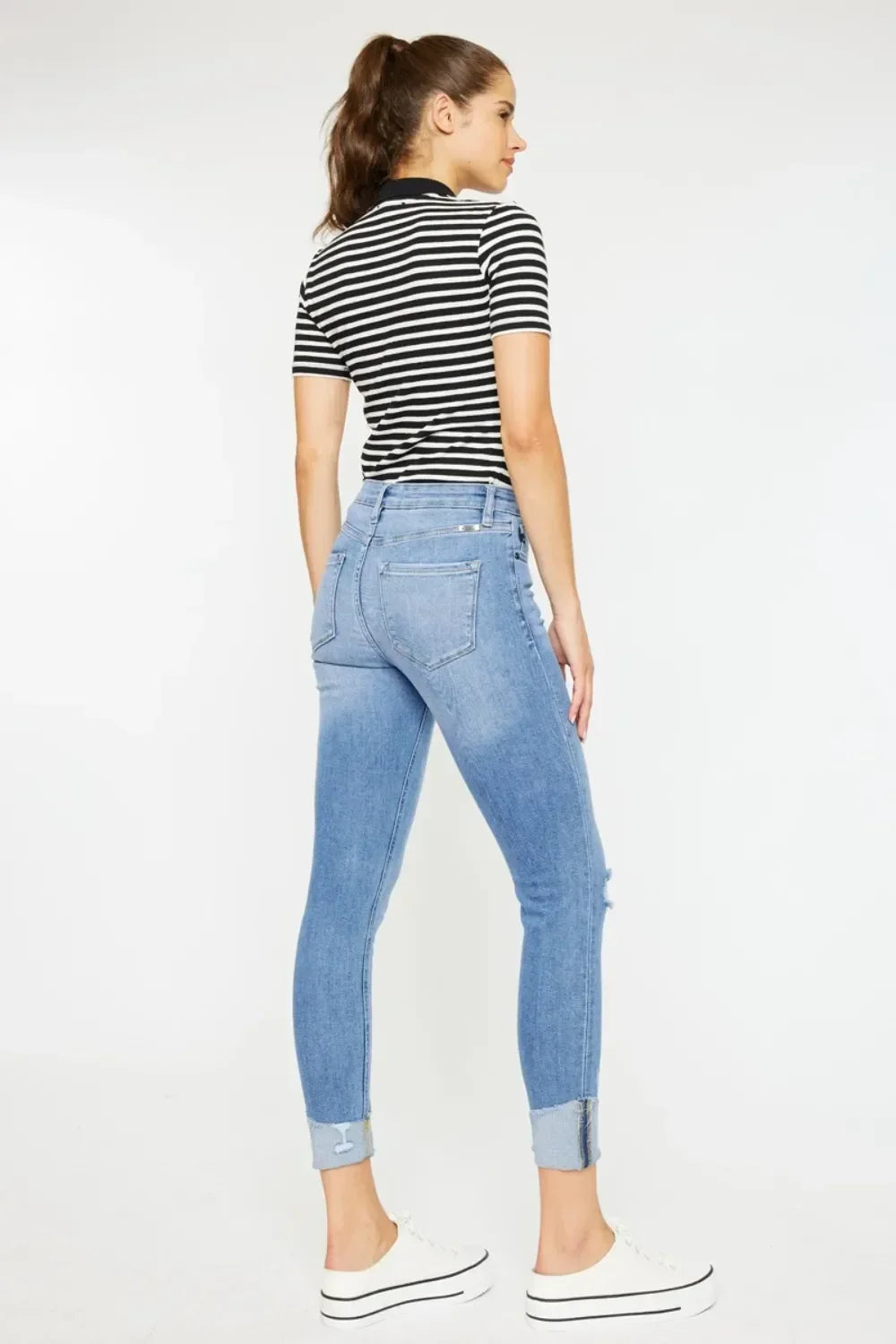 Woman in black and white striped top and light blue cuffed skinny jeans, side view