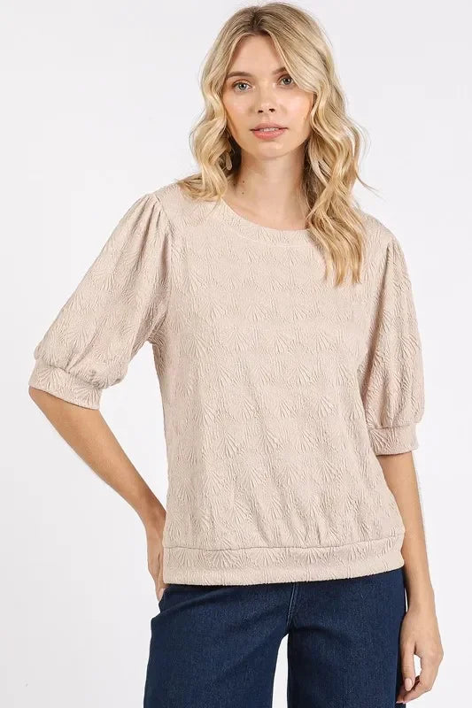Woman wearing a textured beige blouse with puff sleeves and dark blue jeans.