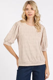 Woman wearing a textured beige blouse with puff sleeves and dark blue jeans.