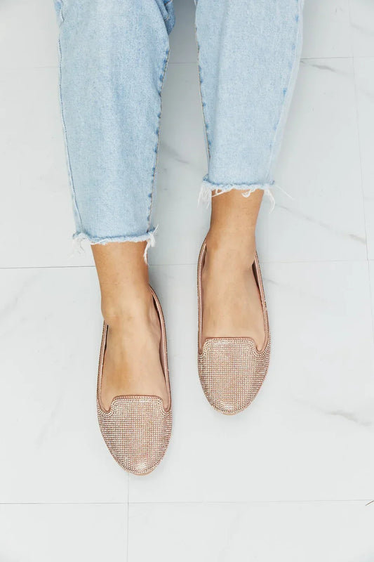Woman wearing light-wash jeans and rose gold rhinestone loafers on white floor