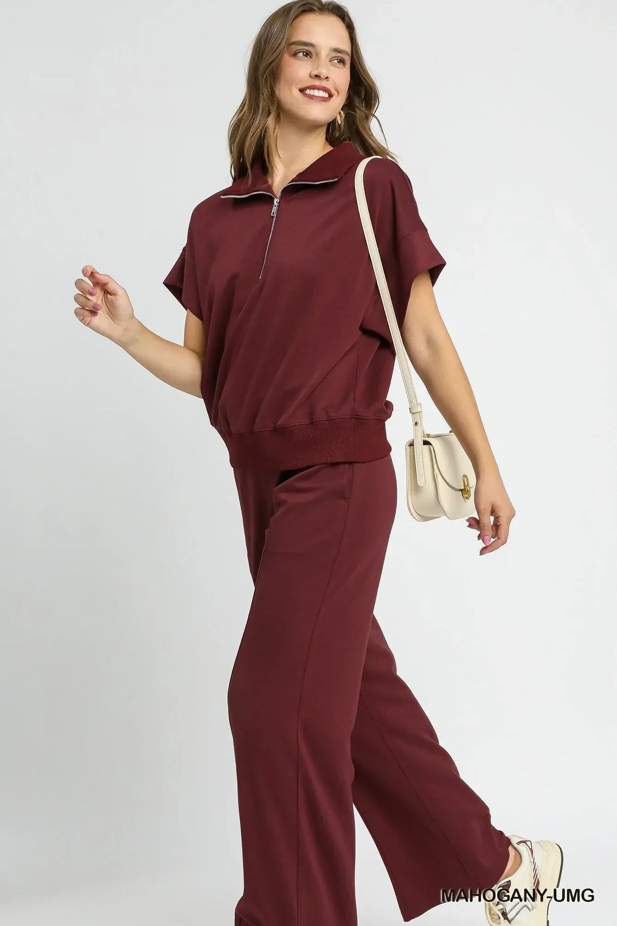 Woman in relaxed burgundy set with half-zip top and wide-leg pants, carrying cream shoulder bag
