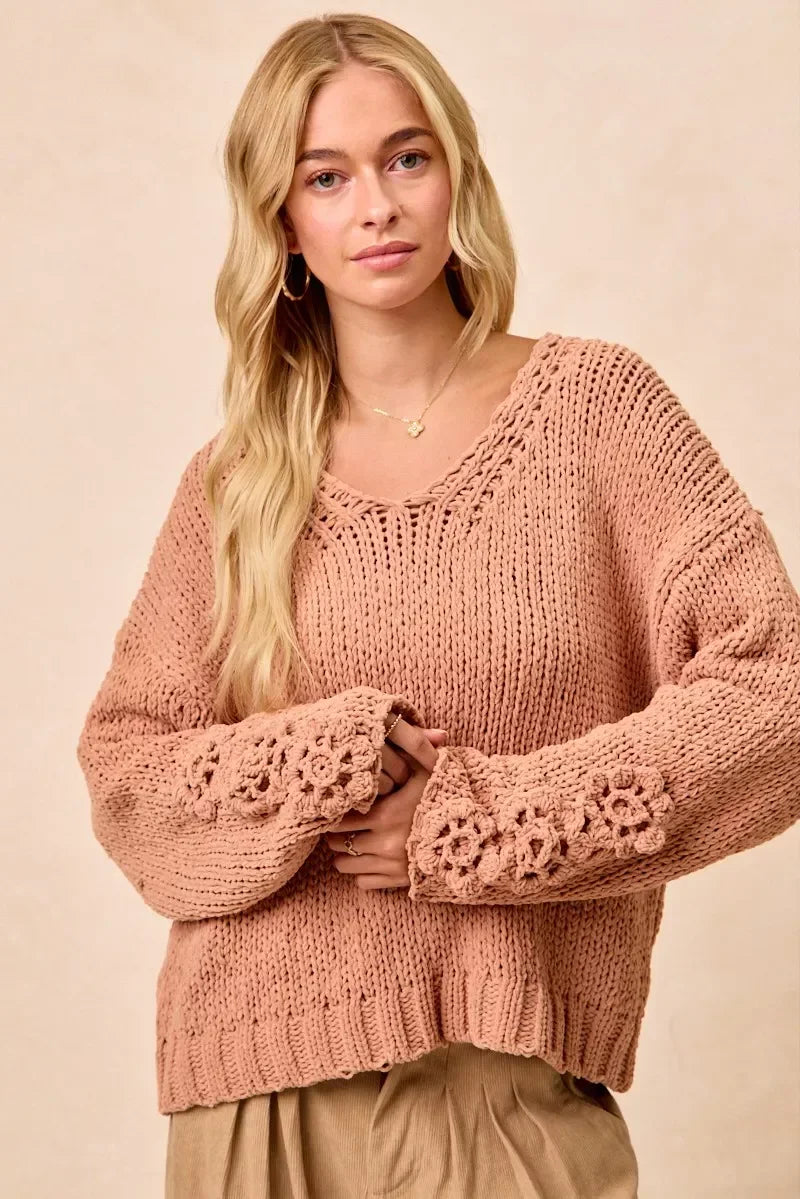 Woman wearing a blush pink chunky knit sweater with floral crochet sleeve details.