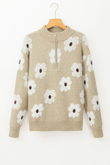 Beige knit pullover sweater with white daisy floral pattern and half-zip collar, hanging on hanger.