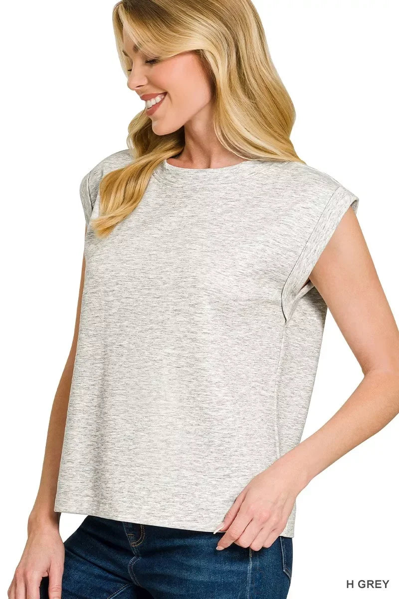 Woman wearing a light heather grey sleeveless top with rolled cuffs and blue jeans