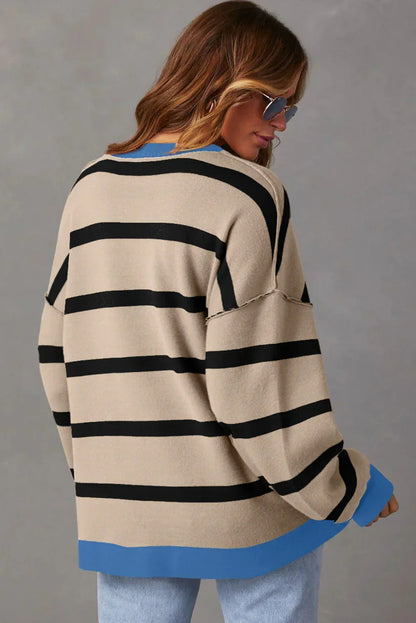 Woman wearing a beige oversized striped sweater with blue trim and light wash jeans