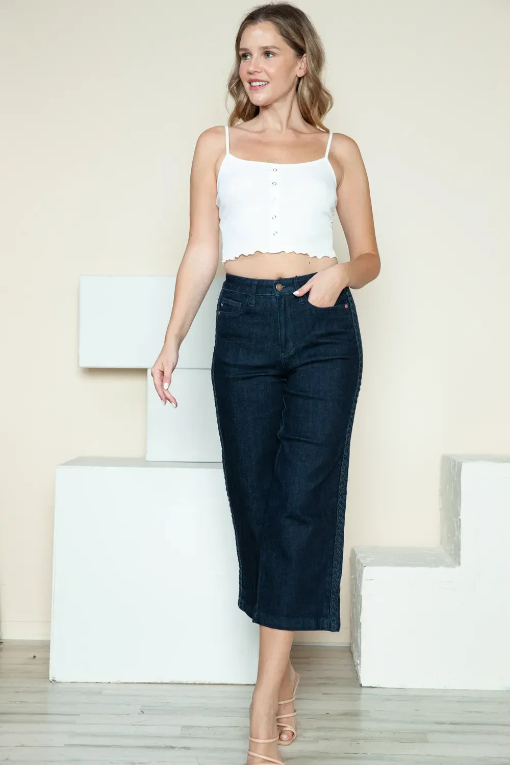 Woman wearing a white cropped tank top and high-waisted dark denim wide-leg jeans