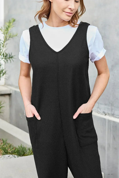 Woman wearing a black sleeveless jumpsuit with front pockets over a white shirt