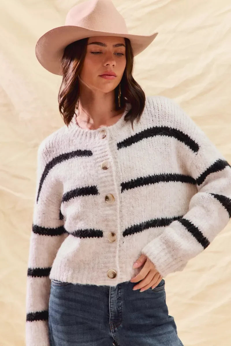 Woman in a beige hat and striped button-up knit cardigan with blue jeans