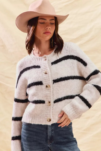 Woman in a beige hat and striped button-up knit cardigan with blue jeans