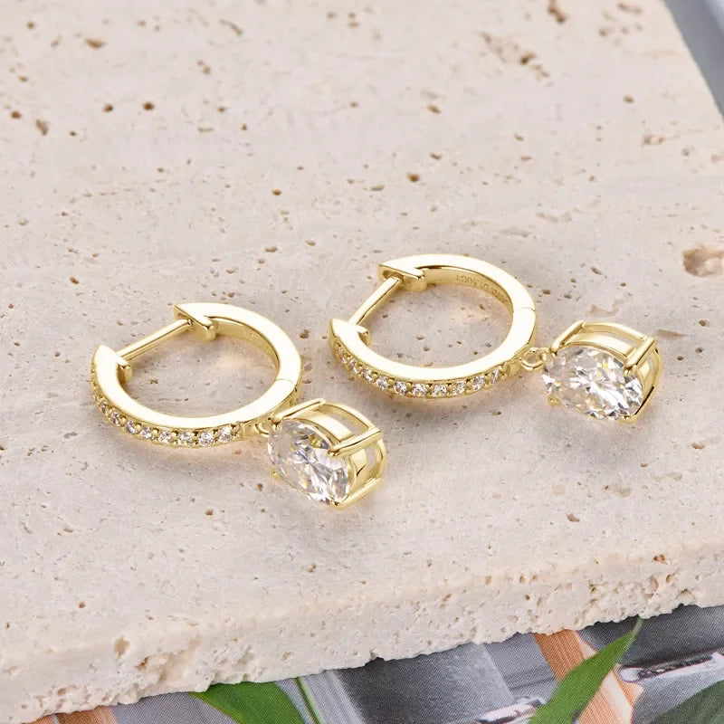 Gold hoop earrings with pavé stones and large oval crystal drop on cream textured surface