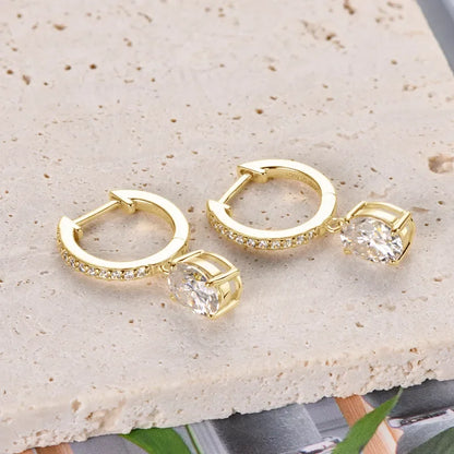 Gold hoop earrings with pavé stones and large oval crystal drop on cream textured surface
