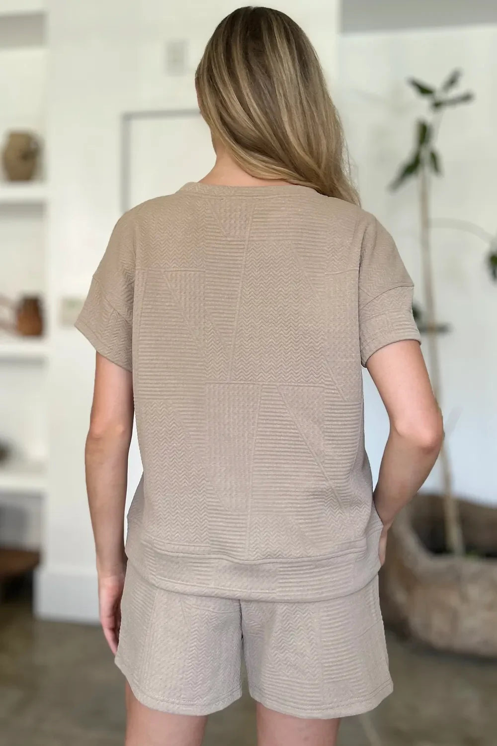 Woman wearing textured beige short sleeve lounge set with shorts, shown from the back.