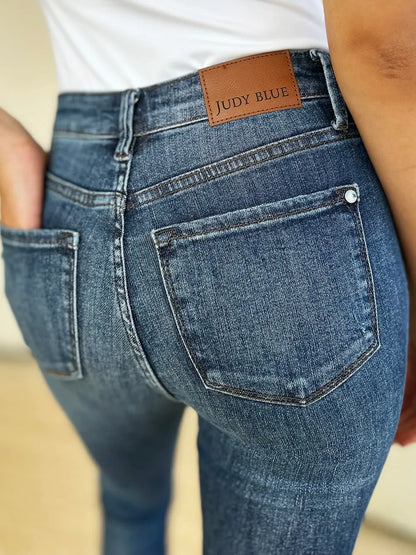 Close-up of high-waisted blue denim jeans with back pockets and leather patch detail.