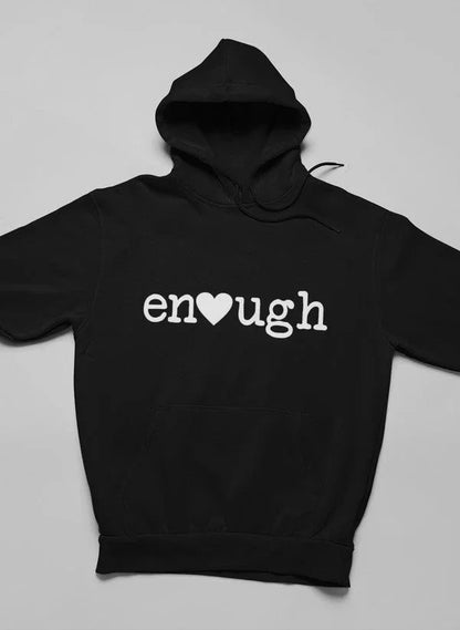Black pullover hoodie with 'enough' and heart graphic on chest, laid flat on neutral background