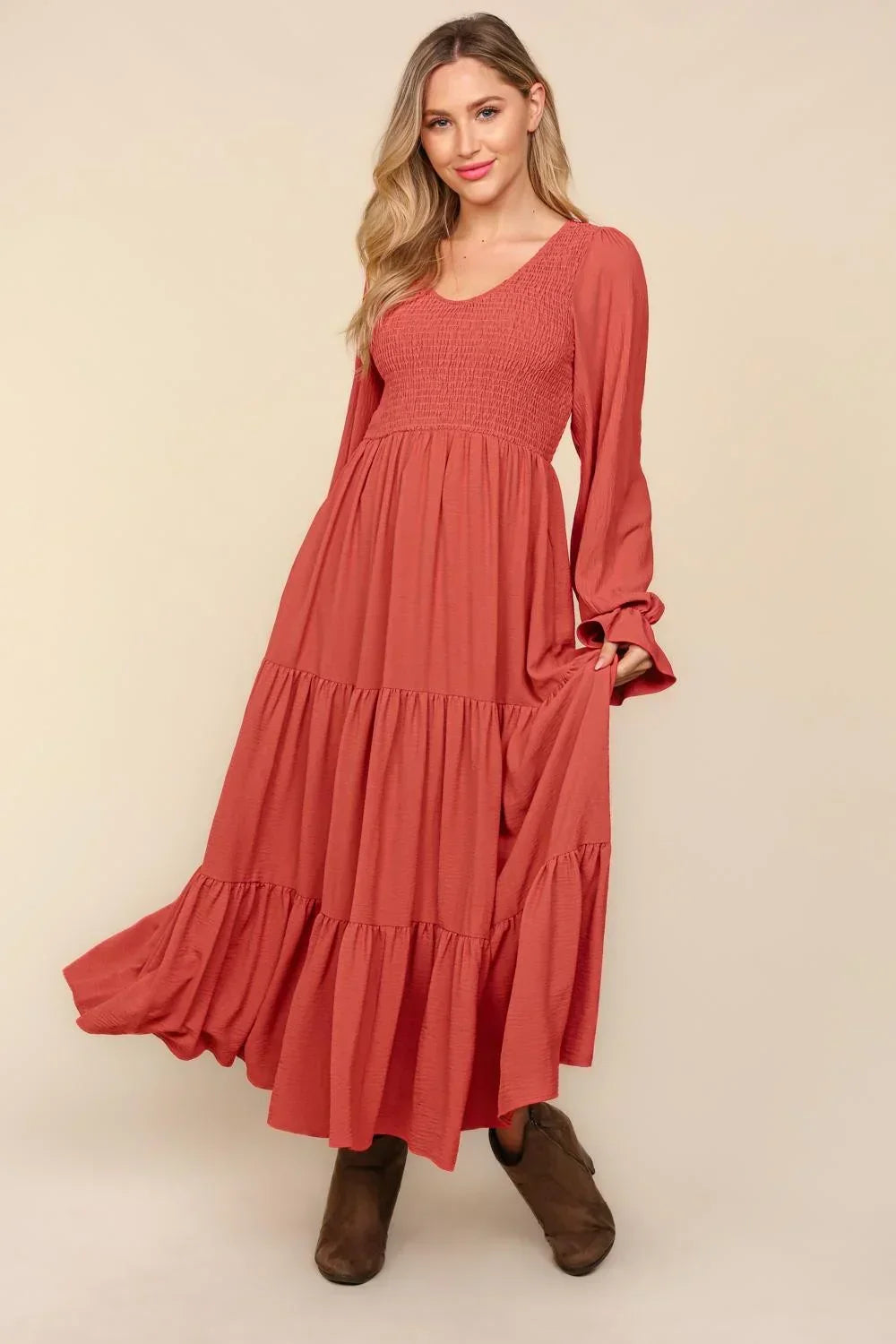 Woman wearing a rust-colored maxi dress with long sleeves and tiered skirt, styled with boots.