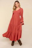 Woman wearing a rust-colored maxi dress with long sleeves and tiered skirt, styled with boots.