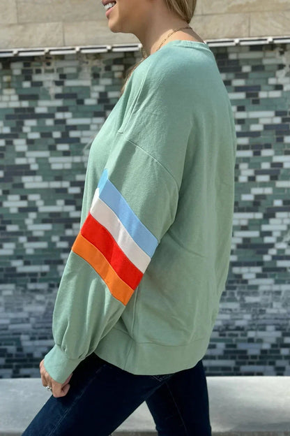 Woman wearing sage green pullover with colorful striped sleeve detail, casual outfit