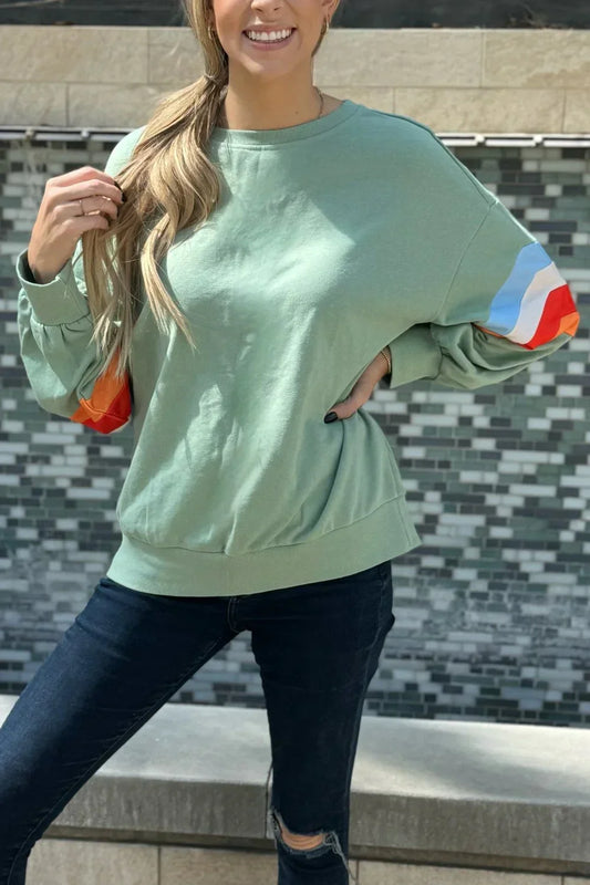 Woman wearing a light green sweatshirt with colorful sleeve stripes and dark skinny jeans