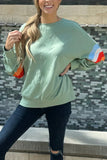 Woman wearing a light green sweatshirt with colorful sleeve stripes and dark skinny jeans