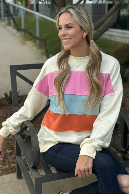 Woman wearing a colorblock sweatshirt with pink, blue, and orange stripes, seated outdoors